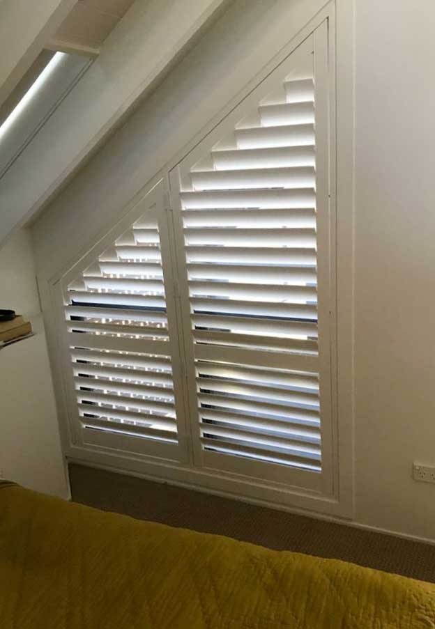 White PVC shutters fitted to an angled bedroom window